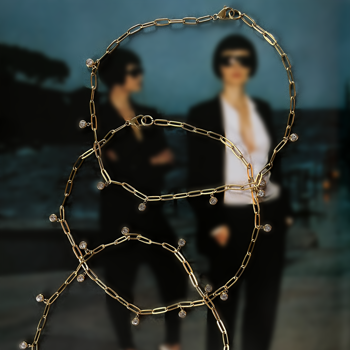 Collar dorado de eslabones con dijes de cristal ROKA sobre fondo editorial desenfocado, joyería de acero inoxidable.